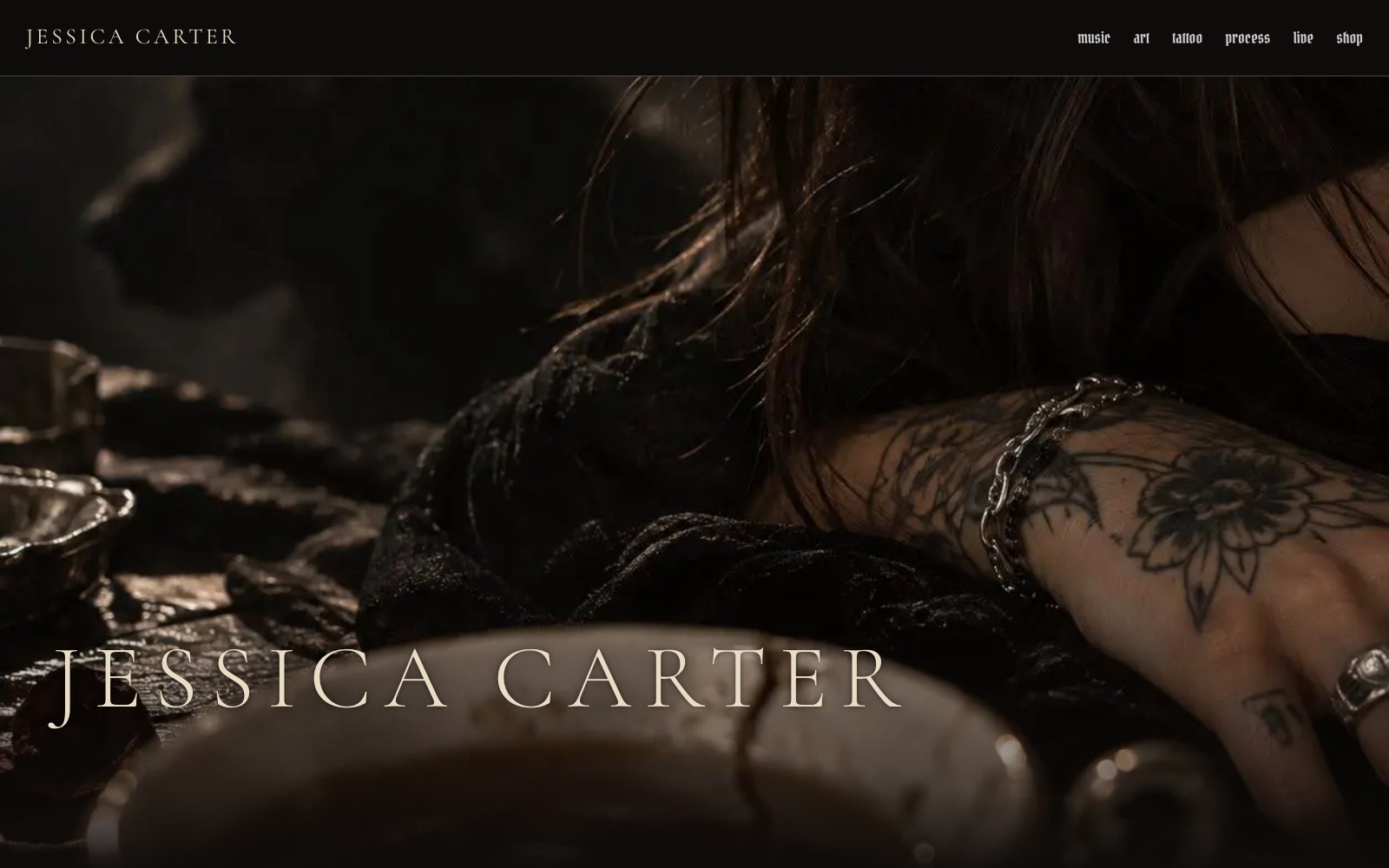 The Jessica Carter home page: her name set large in a pale serif over a dark, close photograph of a tattooed hand and arm resting on a wooden table.